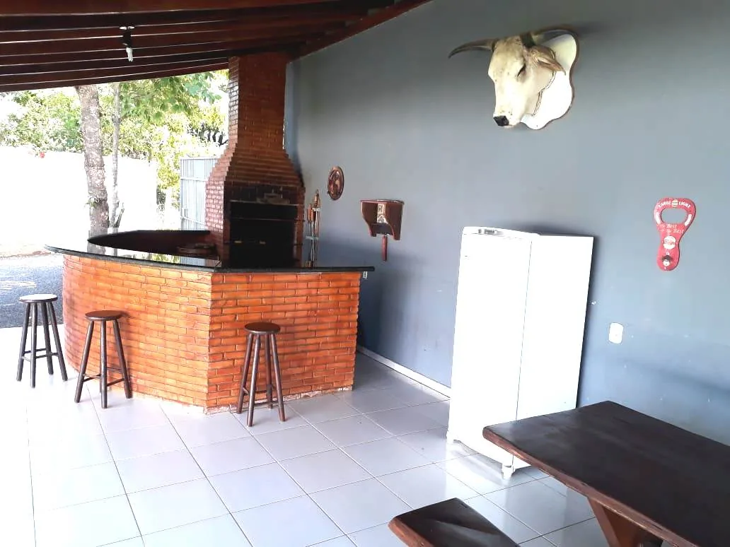 Churrasqueira de tijolo à vista com bar de balcão preto e banquetas de madeira, geladeira e cabeça de boi na parede